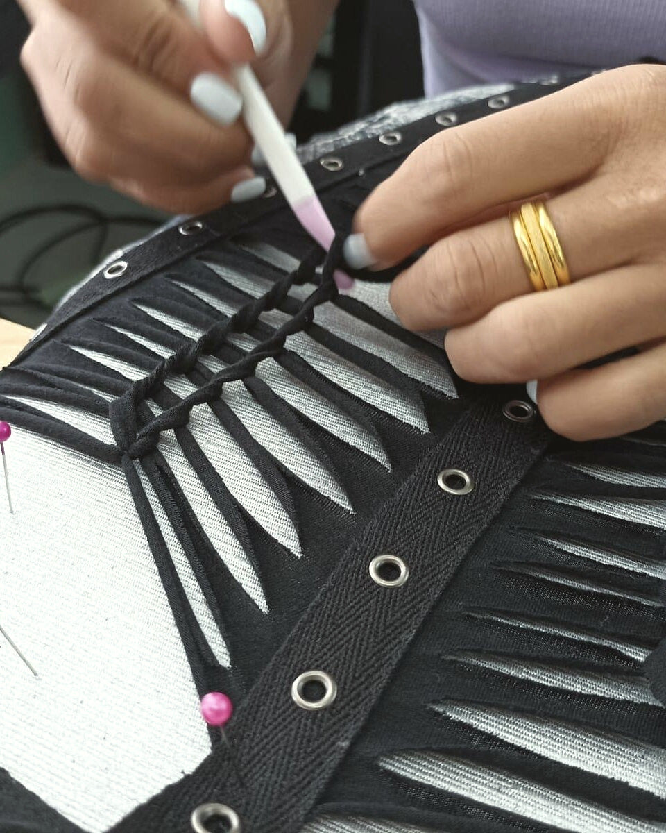 Hands pinning and marking black cut-work fabric with eyelets at the atelier table