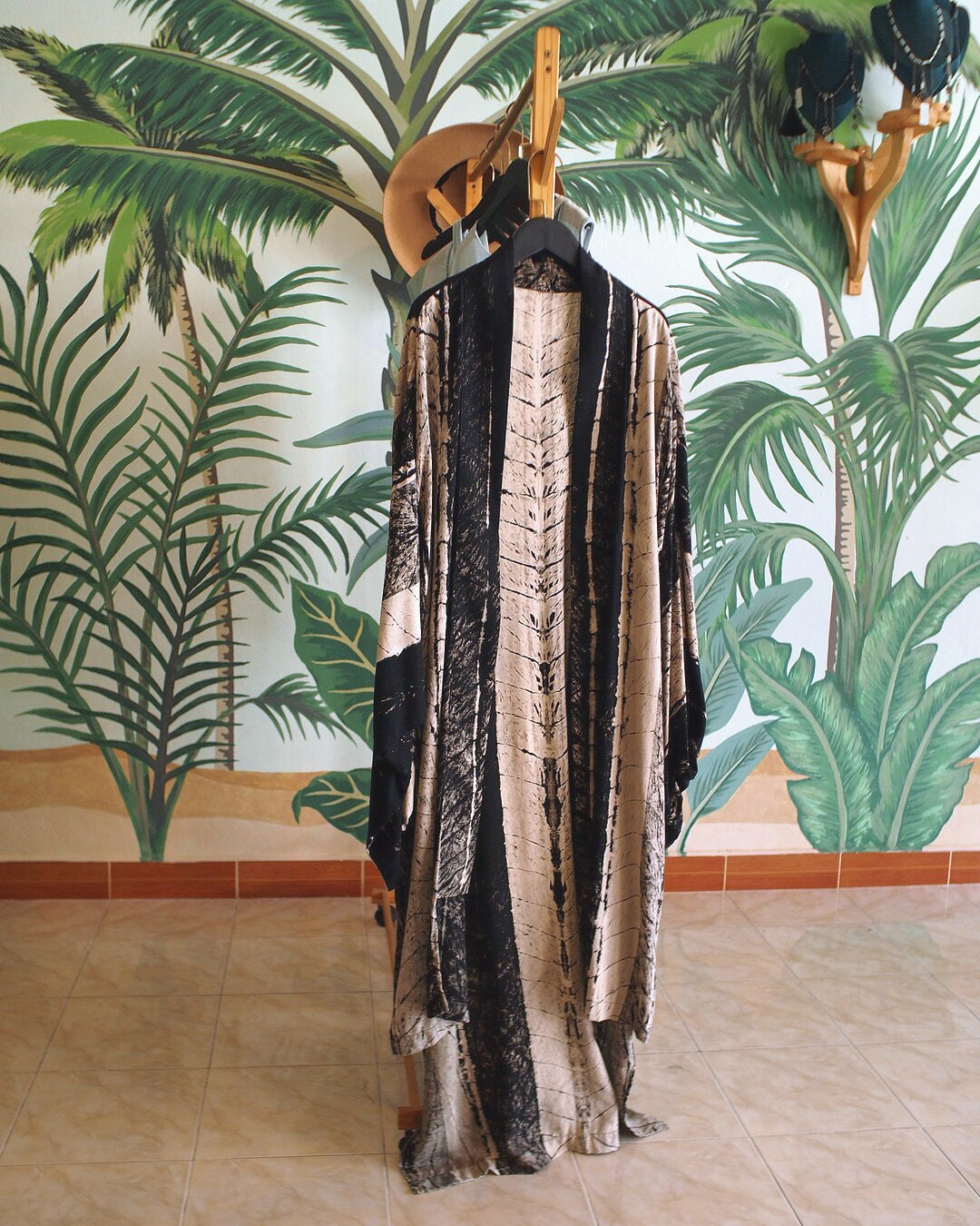 Patterned kimono hanging on a wooden rack against a painted palm wall